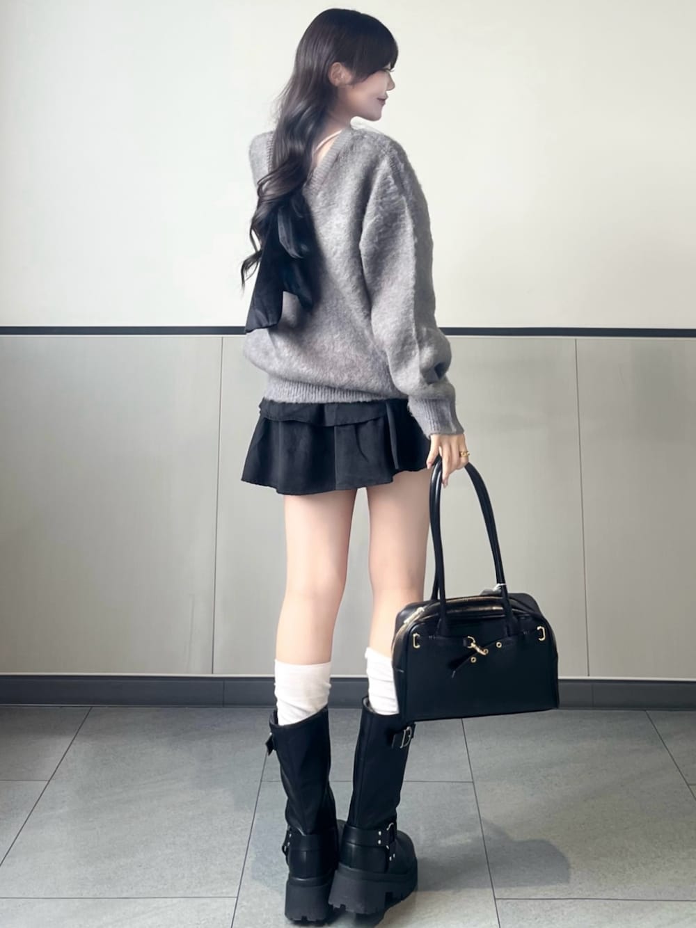 グレー系のニット/セーター、ブラック系のスカート、ブラック系のハンドバッグを着用したレディースの秋コーディネートの1枚目の写真