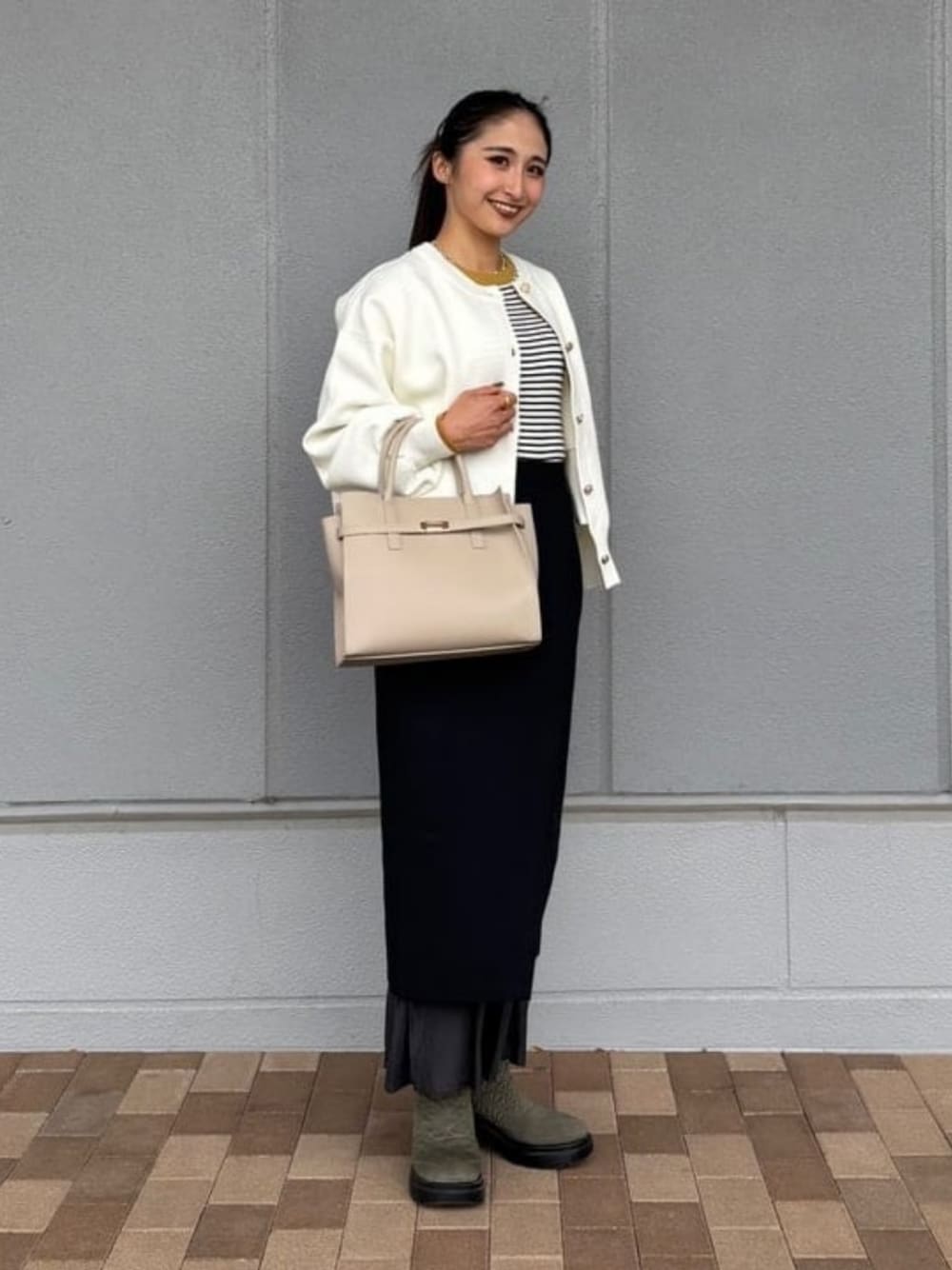 ブラック系のスカート、ベージュ系のショルダーバッグ、ホワイト系のニット/セーターを着用したレディースの冬コーディネートの1枚目の写真