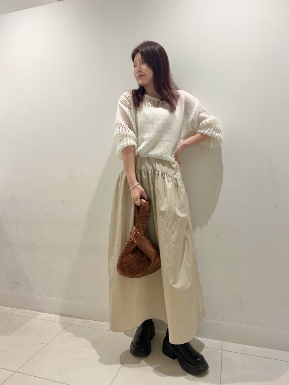 ベージュ系のスカート、ブラック系のブーツ、ホワイト系のニット/セーターを着用したレディースの秋コーディネートの1枚目の写真