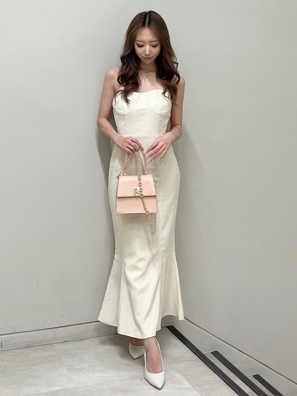 ホワイト系のパンプス、ホワイト系のワンピース、ピンク系のハンドバッグを着用したレディースの春コーディネートの1枚目の写真