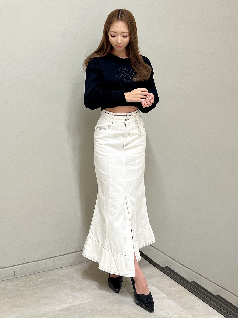 ブラック系のスウェット、ホワイト系のデニムスカート、ブラック系のパンプスを着用したレディースの冬コーディネートの1枚目の写真