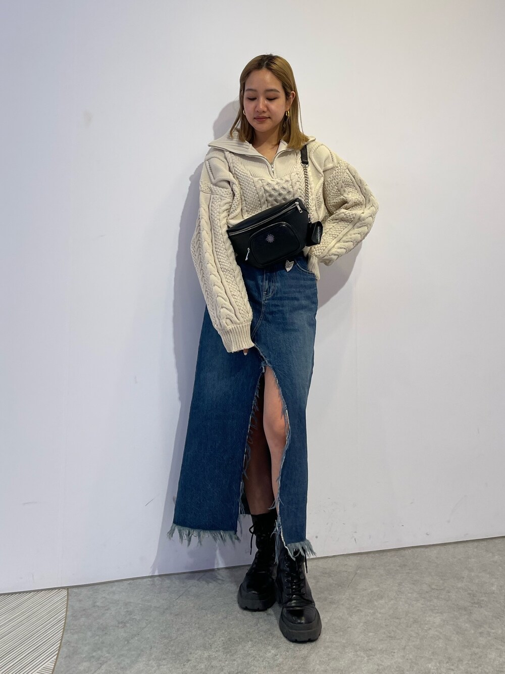 ブルー系のデニムスカート、ブラック系のブーツ、ホワイト系のニット/セーターを着用したレディースの冬コーディネートの1枚目の写真