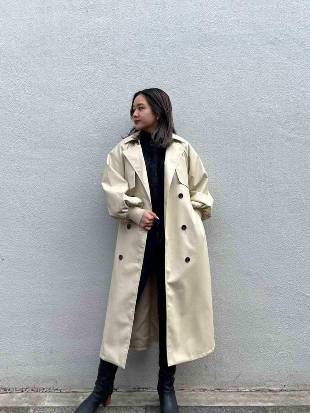 ブラック系のニット/セーター、ホワイト系のトレンチコート、ブラック系のブーツを着用したレディースの冬コーディネートの1枚目の写真