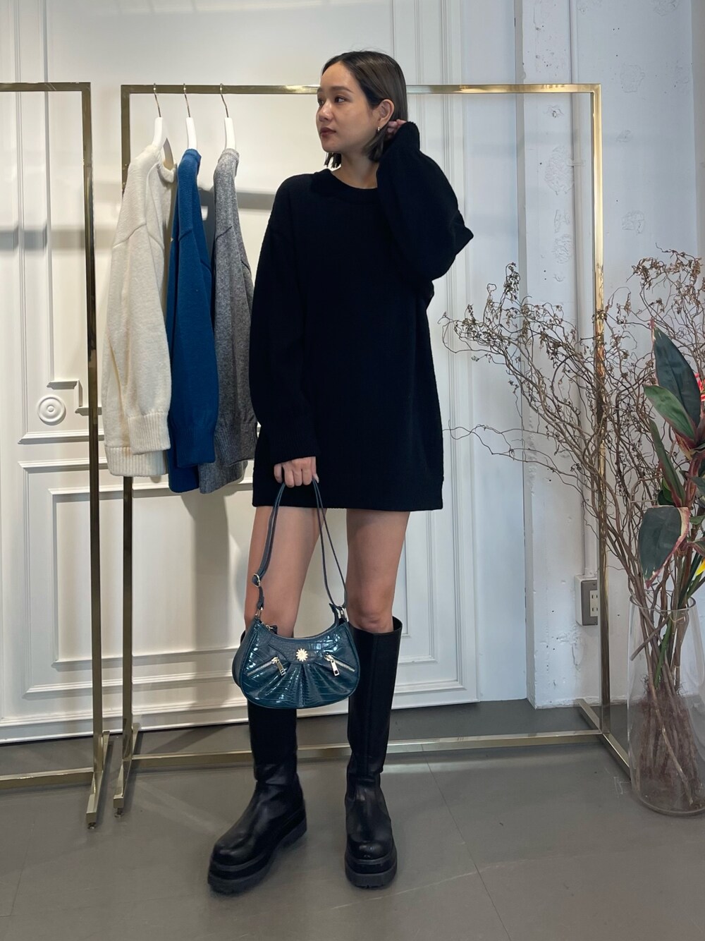 ブラック系のニット/セーター、ブルー系のショルダーバッグ、ブラック系のブーツを着用したレディースの秋コーディネートの1枚目の写真