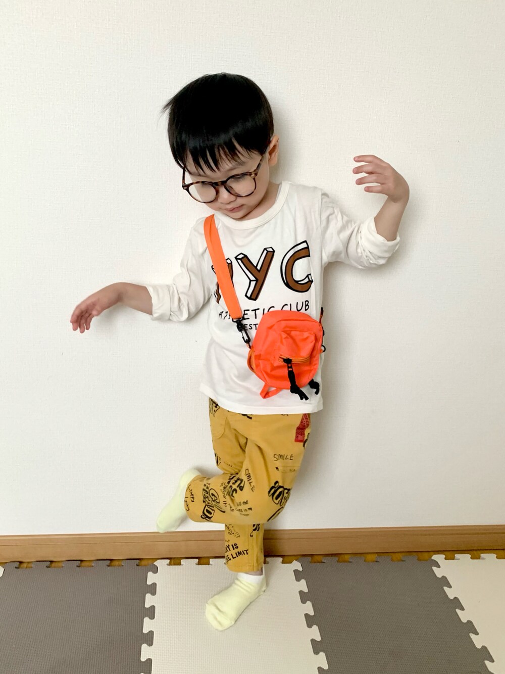 オレンジ系のショルダーバッグ、イエロー系のその他パンツ、ホワイト系のTシャツ/カットソーを着用したキッズの春コーディネートの1枚目の写真