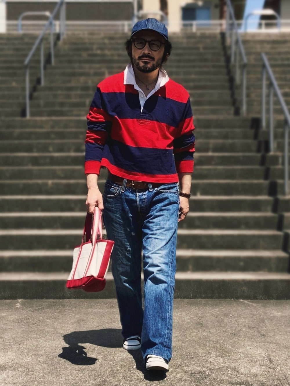 レッド系のポロシャツ、ブルー系のデニムパンツ、ブラック系のスニーカーを着用したメンズの春コーディネートの1枚目の写真