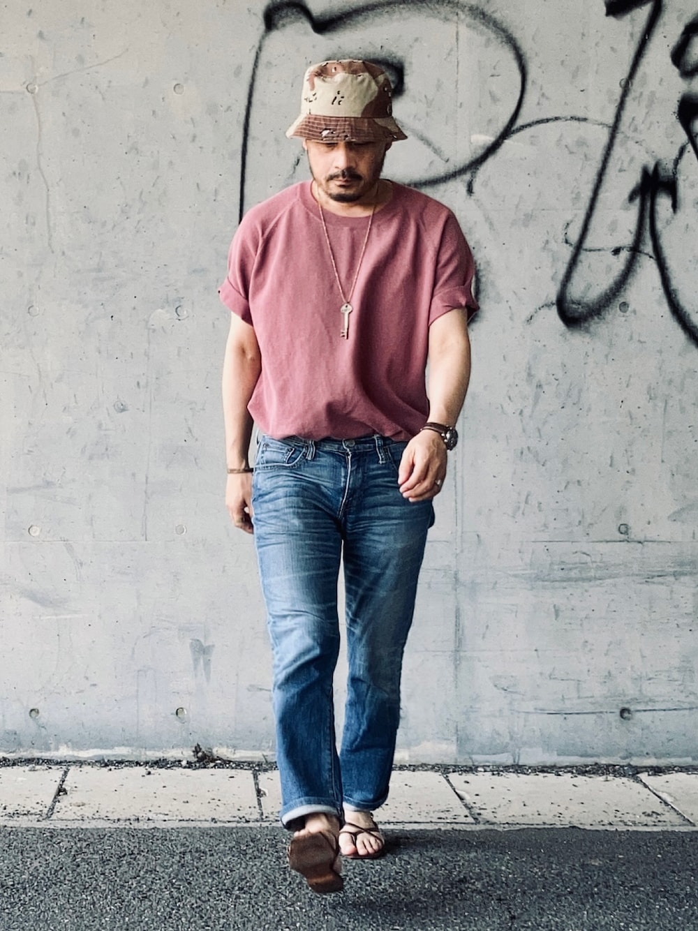 ピンク系のTシャツ/カットソー、ブルー系のデニムパンツ、ブラウン系のサンダルを着用したメンズの夏コーディネートの1枚目の写真