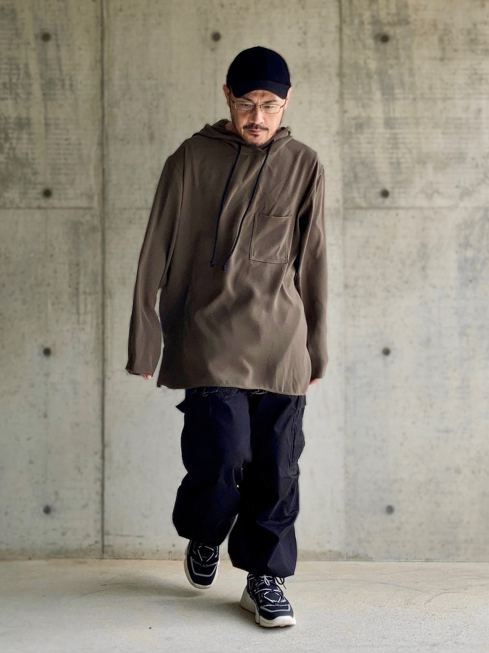 グレー系のパーカー、ブラック系のカーゴパンツ、ブラック系のスニーカーを着用したメンズの秋コーディネートの1枚目の写真