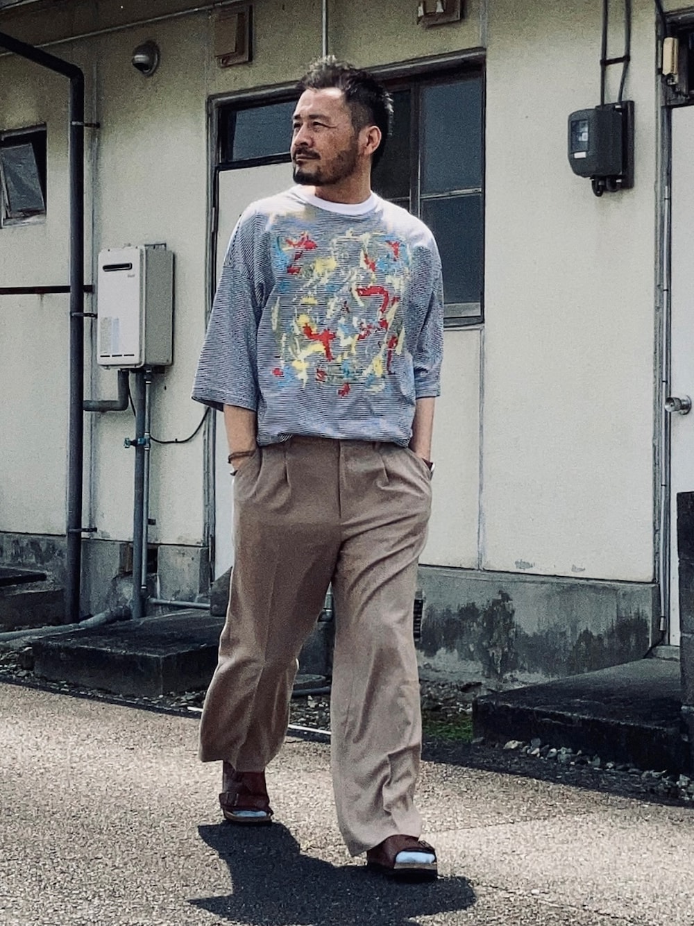 ホワイト系のTシャツ/カットソー、ベージュ系のスラックス、ブラウン系のサンダルを着用したメンズの春コーディネートの1枚目の写真