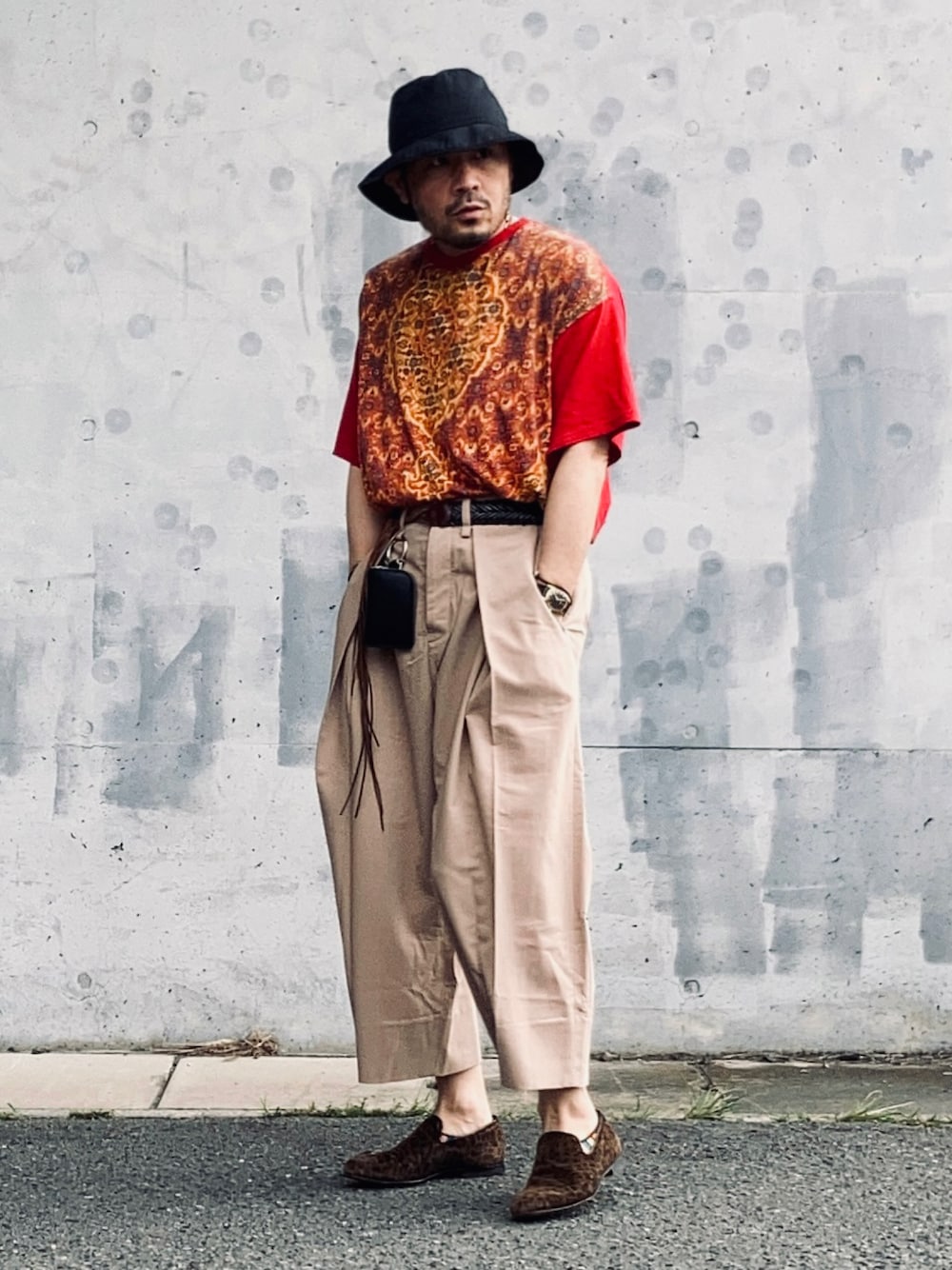 レッド系のTシャツ/カットソー、ベージュ系のスラックス、ブラウン系のスリッポンを着用したメンズの春コーディネートの1枚目の写真