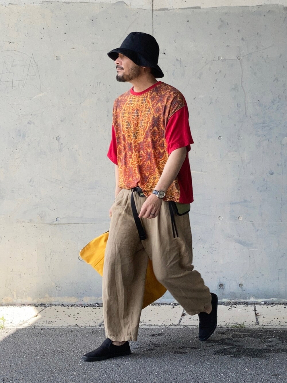 レッド系のTシャツ/カットソー、ベージュ系のその他パンツ、ブラック系のスリッポンを着用したメンズの春コーディネートの1枚目の写真