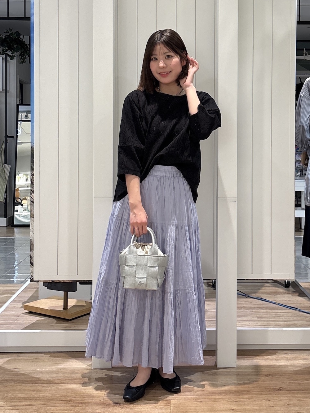ブルー系のスカート、ブラック系のパンプス、シルバー系のトートバッグを着用したレディースの春コーディネートの1枚目の写真