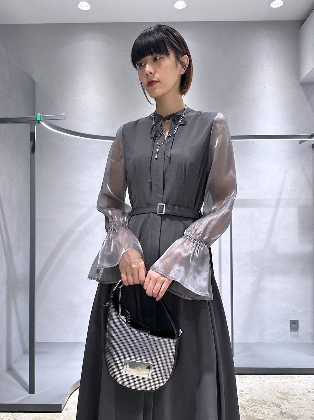 シルバー系のハンドバッグ、ブラック系のブーツ、グレー系のドレスを着用したレディースの秋コーディネートの1枚目の写真