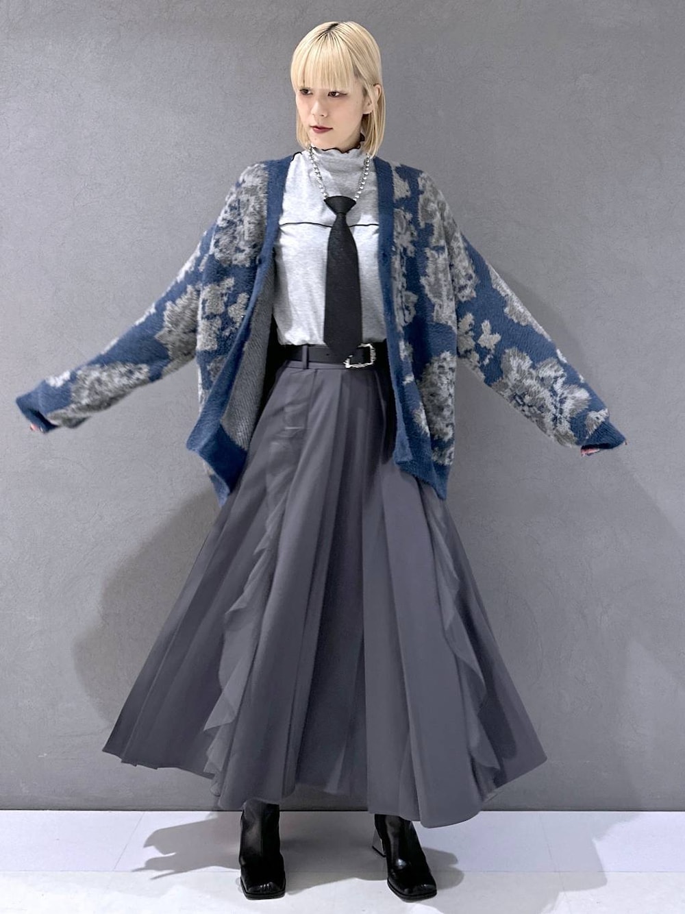 ブラック系のネクタイ、ブルー系のカーディガン/ボレロ、ブラック系のブーツを着用したレディースの秋コーディネートの1枚目の写真