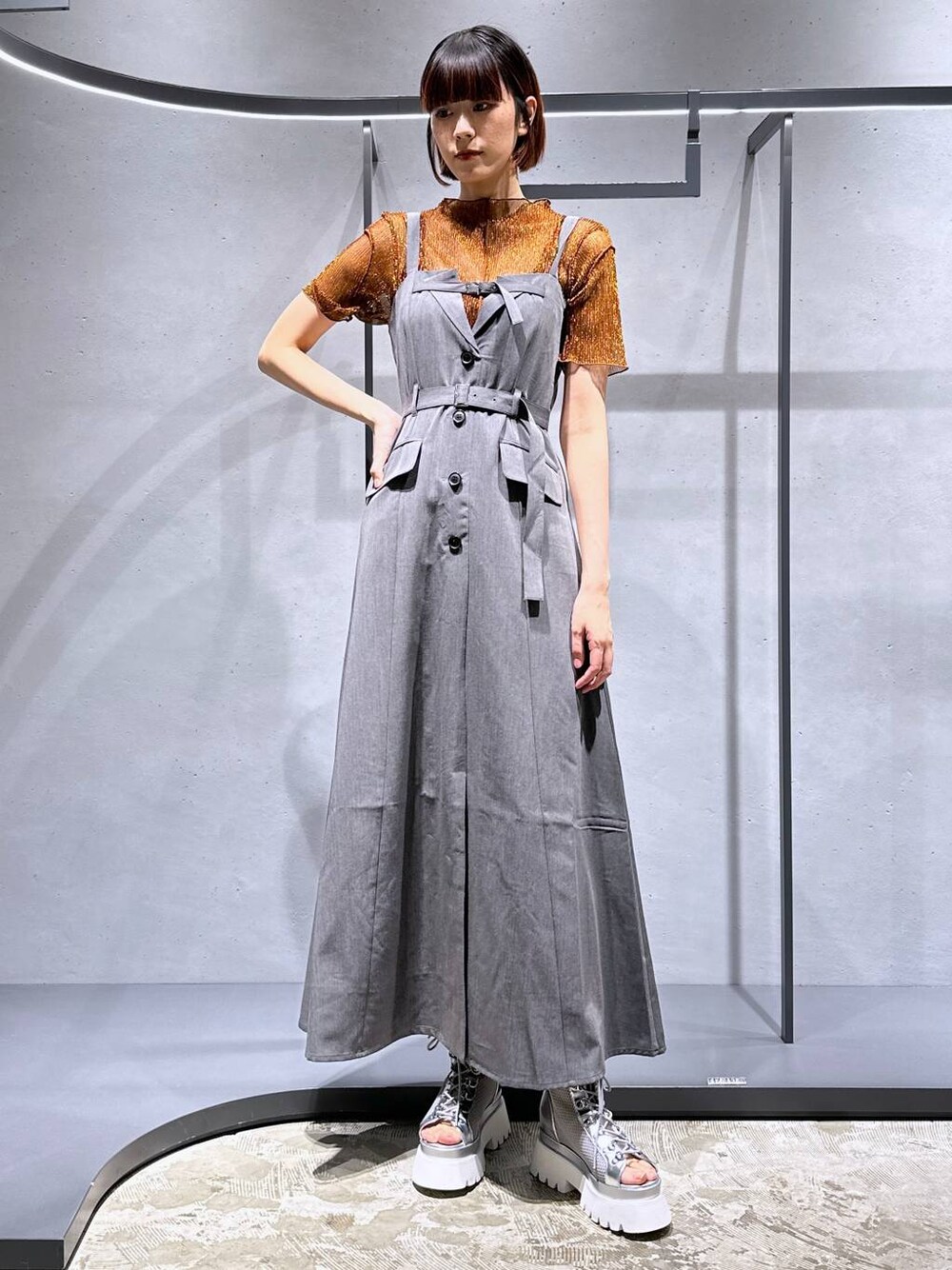 シルバー系のサンダル、オレンジ系のTシャツ/カットソー、グレー系のジャンパースカートを着用したレディースの夏コーディネートの1枚目の写真