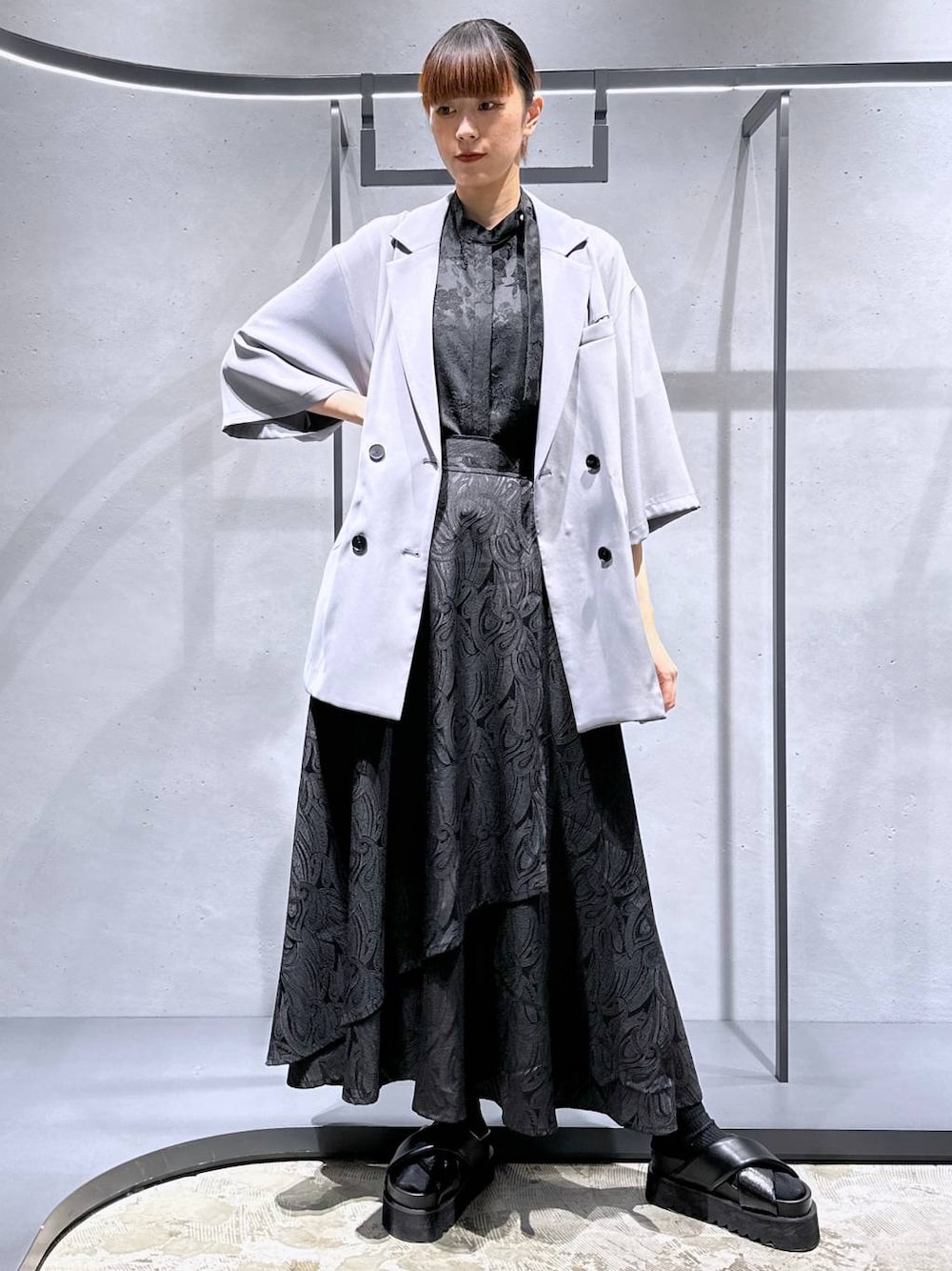 ブラック系のサンダル、ブラック系のスカート、グレー系のテーラードジャケットを着用したレディースの春コーディネートの1枚目の写真