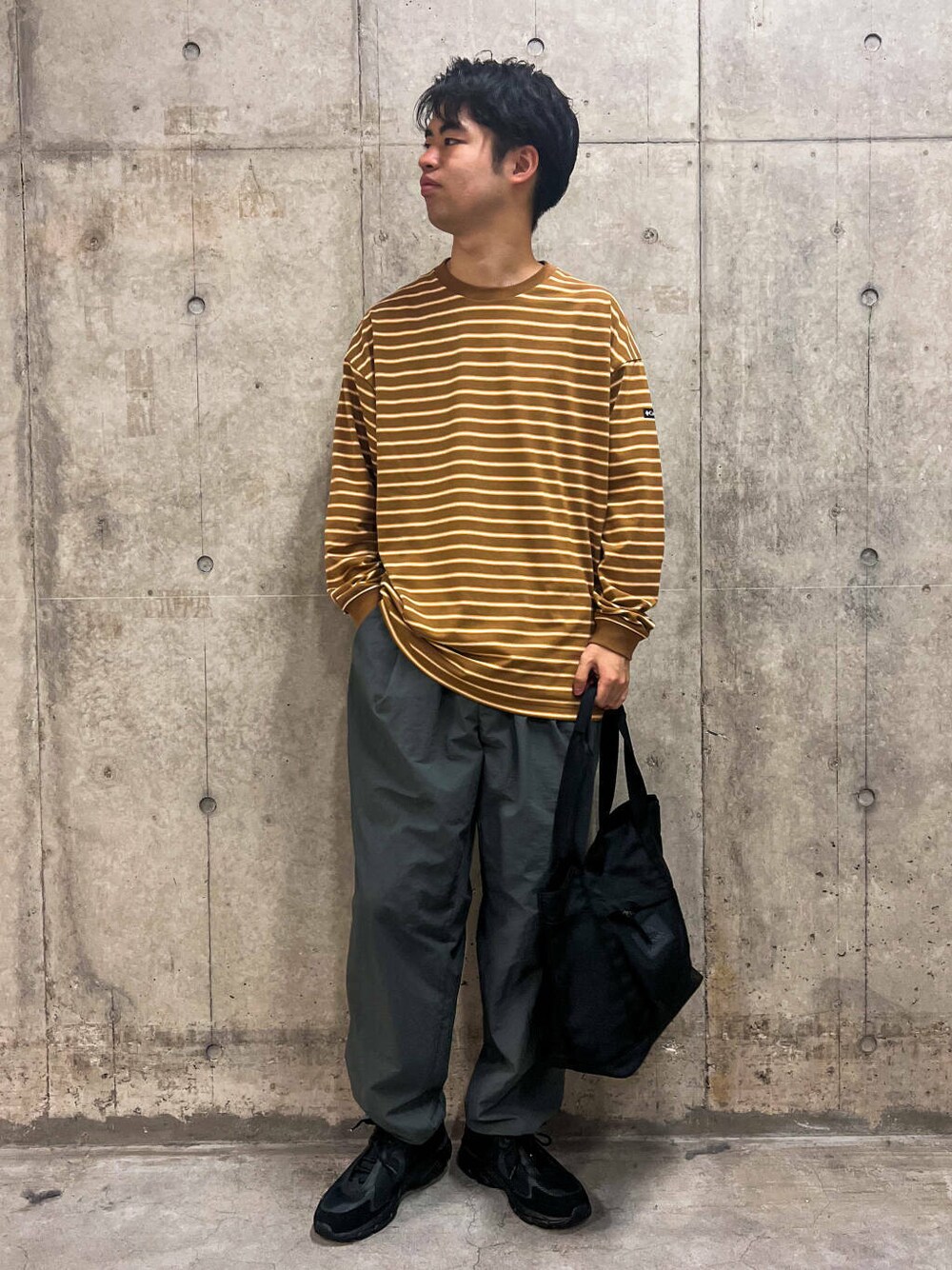 グレー系のその他パンツ、ブラック系のトートバッグ、ベージュ系のTシャツ/カットソーを着用したメンズの秋コーディネートの1枚目の写真