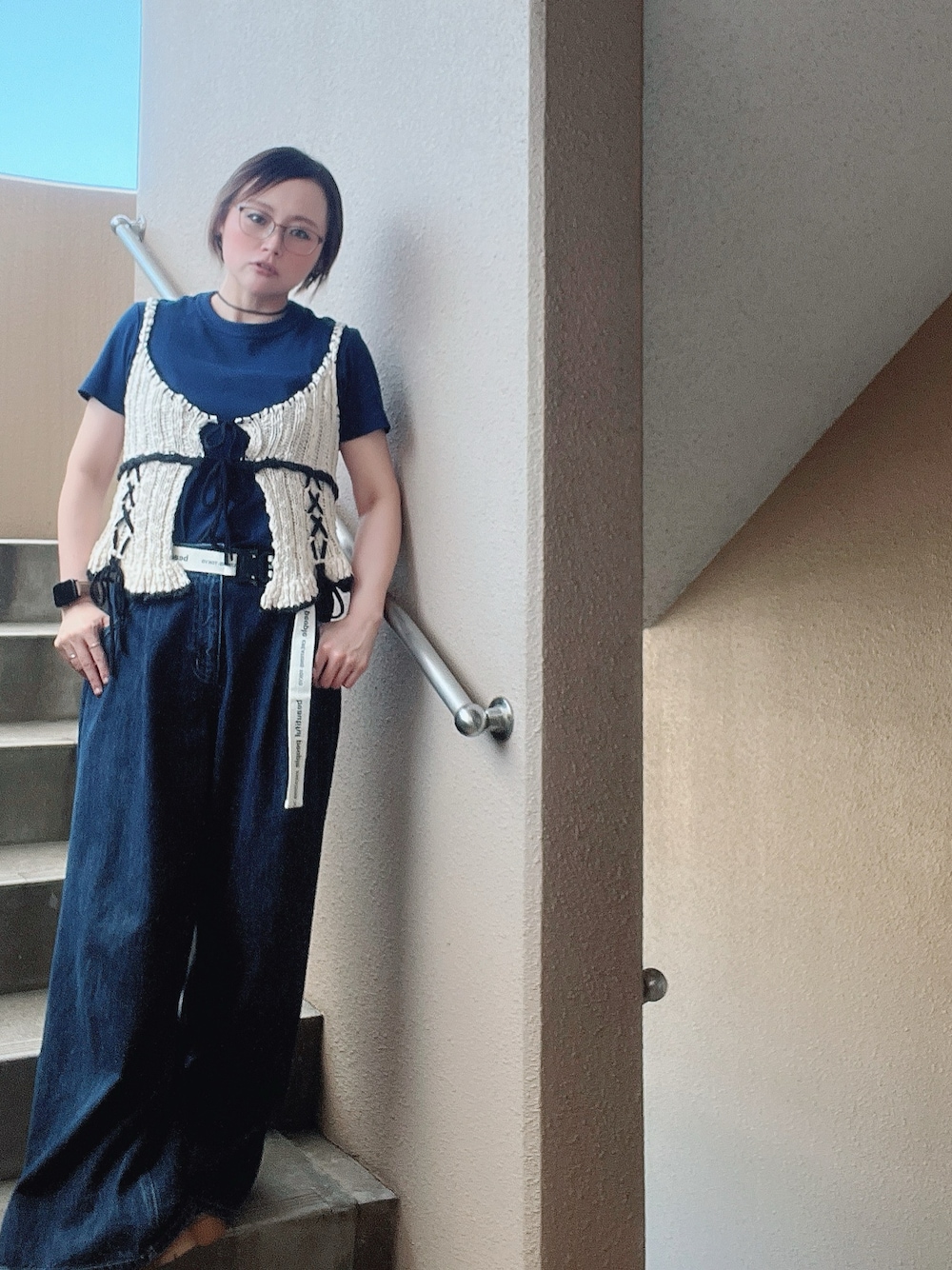 ブルー系のデニムパンツ、ホワイト系のベスト、ブラック系のスニーカーを着用したレディースの秋コーディネートの1枚目の写真