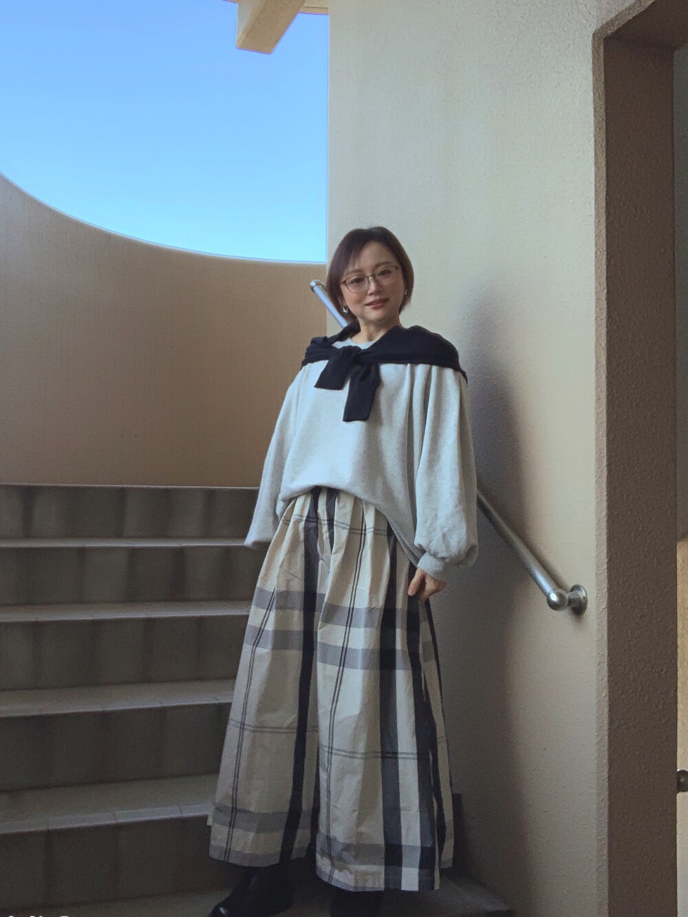 グレー系のスウェット、ブラック系のカーディガン/ボレロ、ホワイト系のスカートを着用したレディースの春コーディネートの1枚目の写真