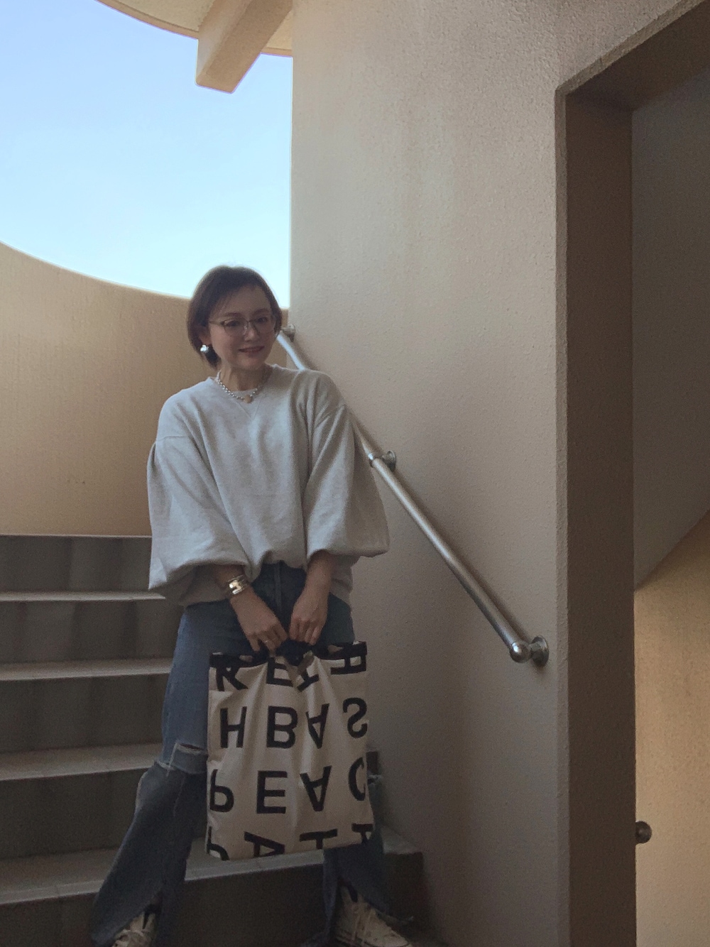 グレー系のスウェット、ブルー系のデニムパンツ、ホワイト系のスニーカーを着用したレディースの春コーディネートの1枚目の写真