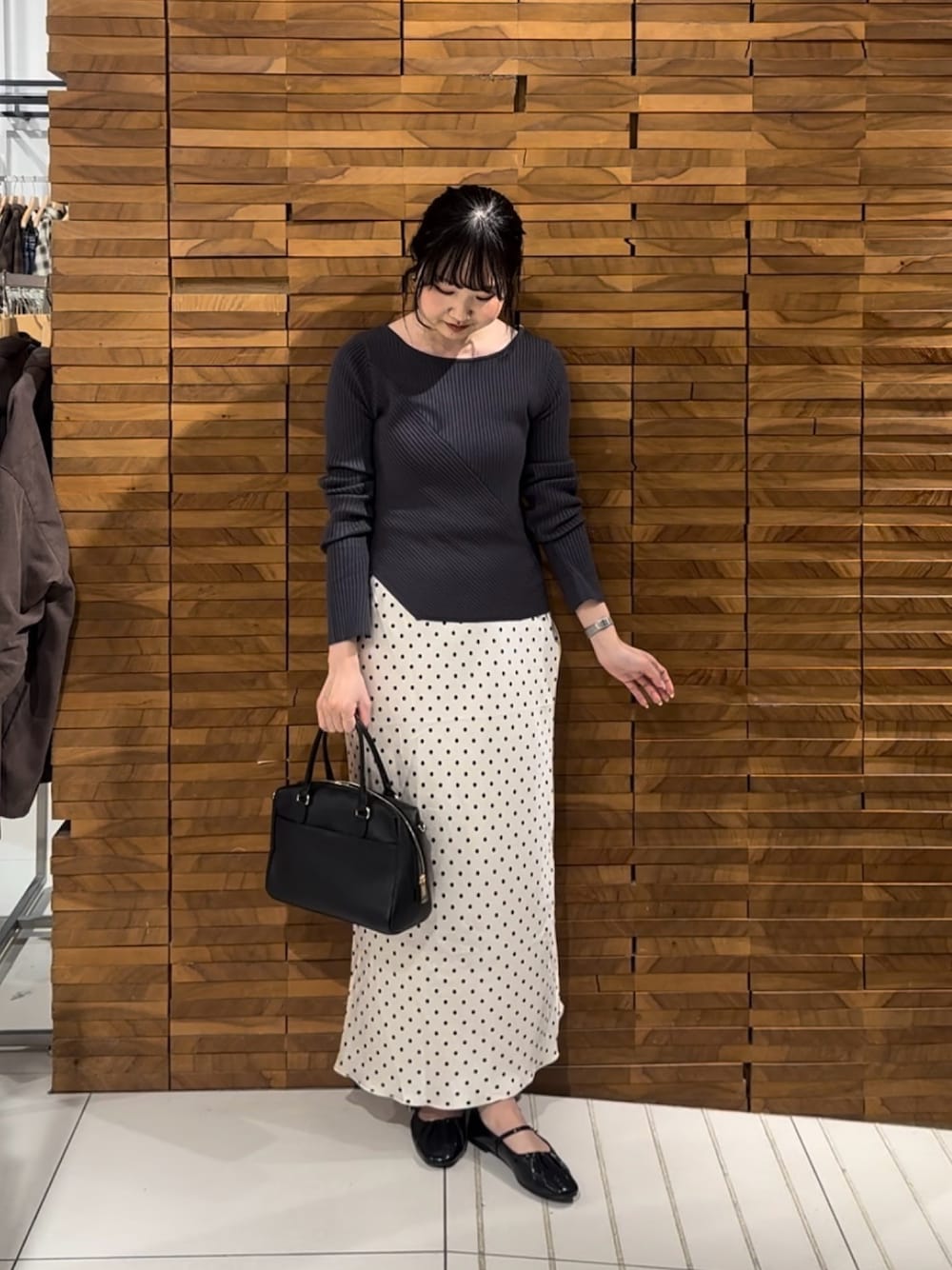 グレー系のニット/セーター、ホワイト系のスカート、ブラック系のパンプスを着用したレディースの春コーディネートの1枚目の写真