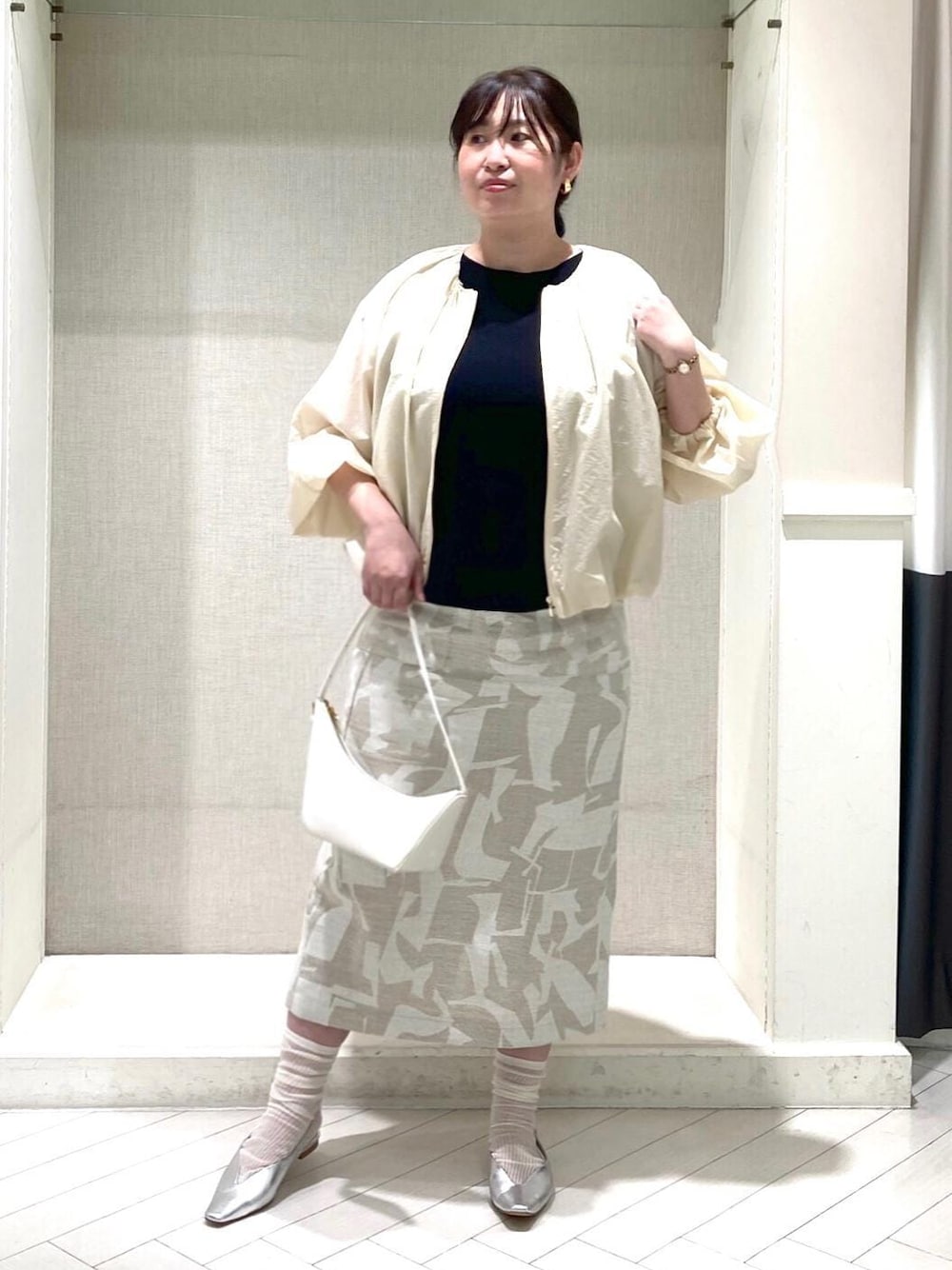 ホワイト系のハンドバッグ、シルバー系のパンプス、ブラック系のニット/セーターを着用したレディースの春コーディネートの1枚目の写真