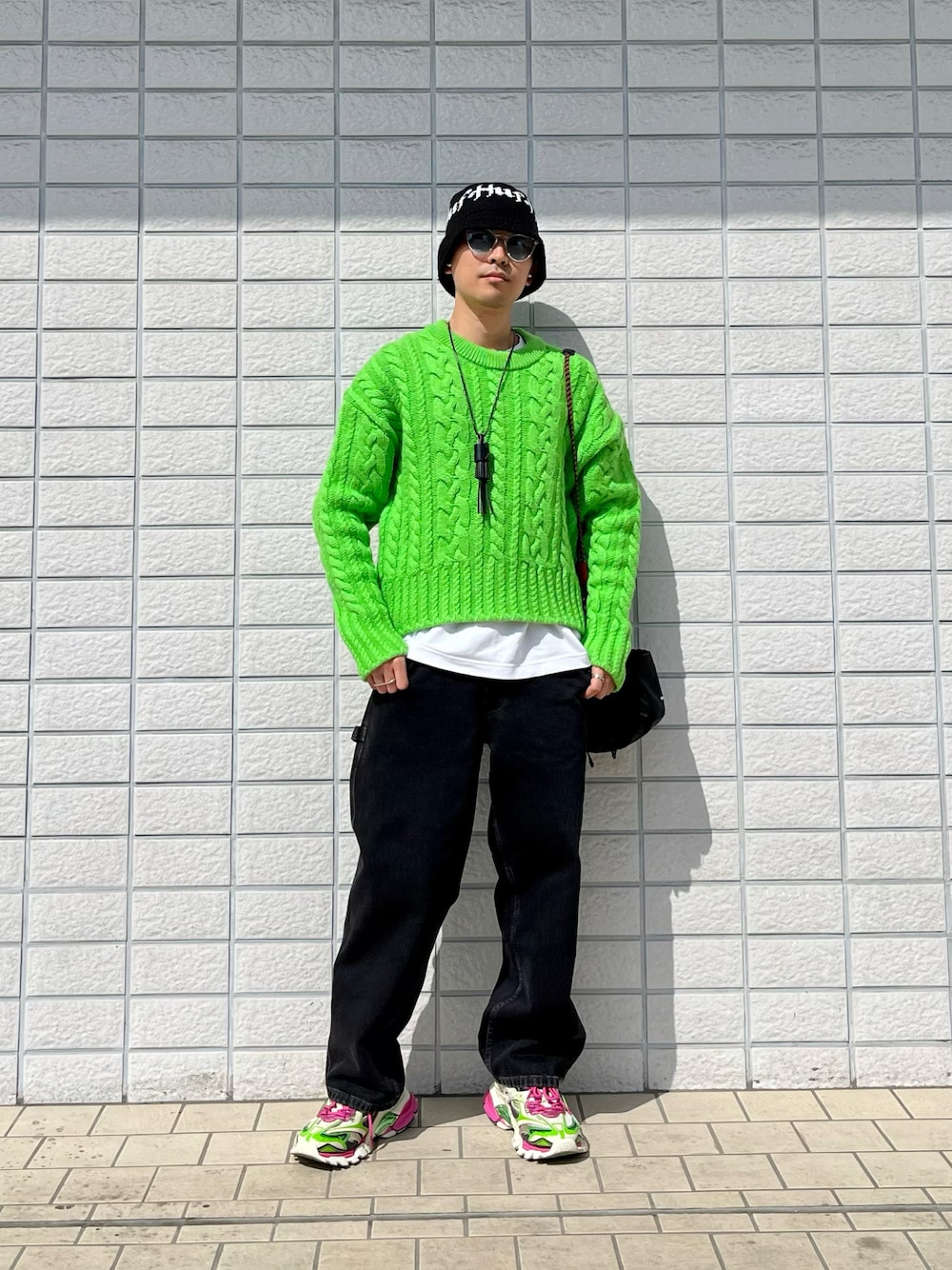 グリーン系のニット/セーター、ブラック系のデニムパンツ、ピンク系のスニーカーを着用したメンズの春コーディネートの1枚目の写真