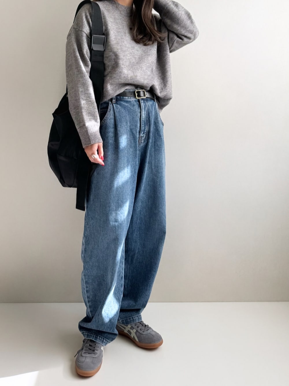 グレー系のニット/セーター、ブルー系のデニムパンツ、ブラック系のショルダーバッグを着用したレディースの秋コーディネートの1枚目の写真