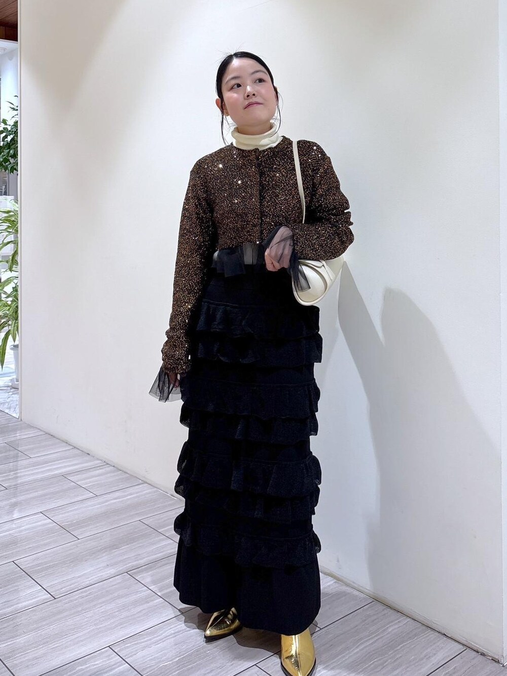 ゴールド系のブーツ、ホワイト系のショルダーバッグ、ブラック系のスカートを着用したレディースの秋コーディネートの1枚目の写真