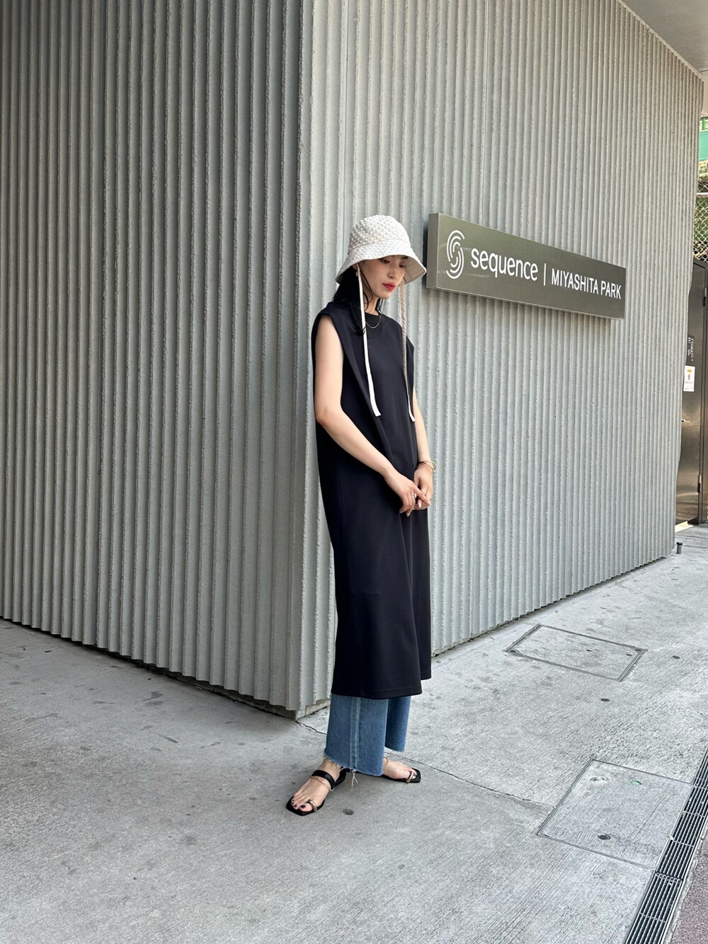 ブラック系のワンピース、ブルー系のデニムパンツ、ブラック系のサンダルを着用したレディースの春コーディネートの1枚目の写真