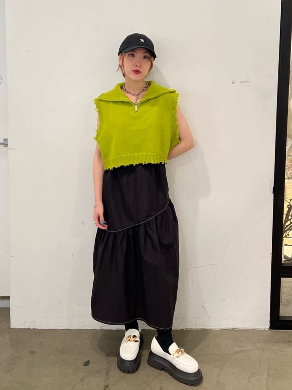 ホワイト系のローファー、グリーン系のベスト、ブラック系のジャンパースカートを着用したレディースの秋コーディネートの1枚目の写真