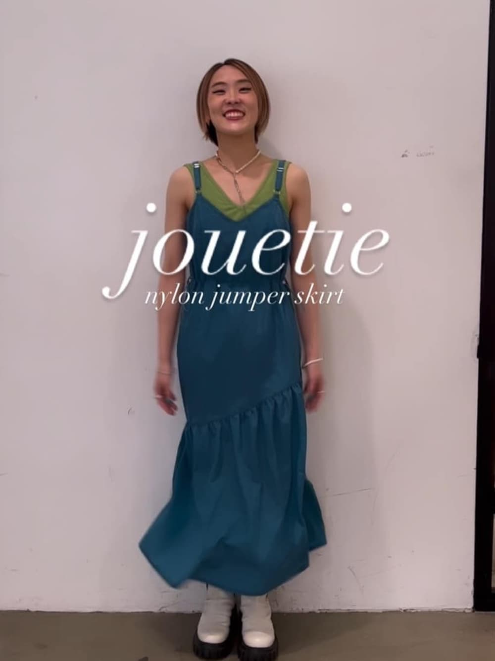 ホワイト系のブーツ、ブルー系のジャンパースカート、グリーン系のキャミソールを着用したレディースの秋コーディネートの1枚目の写真