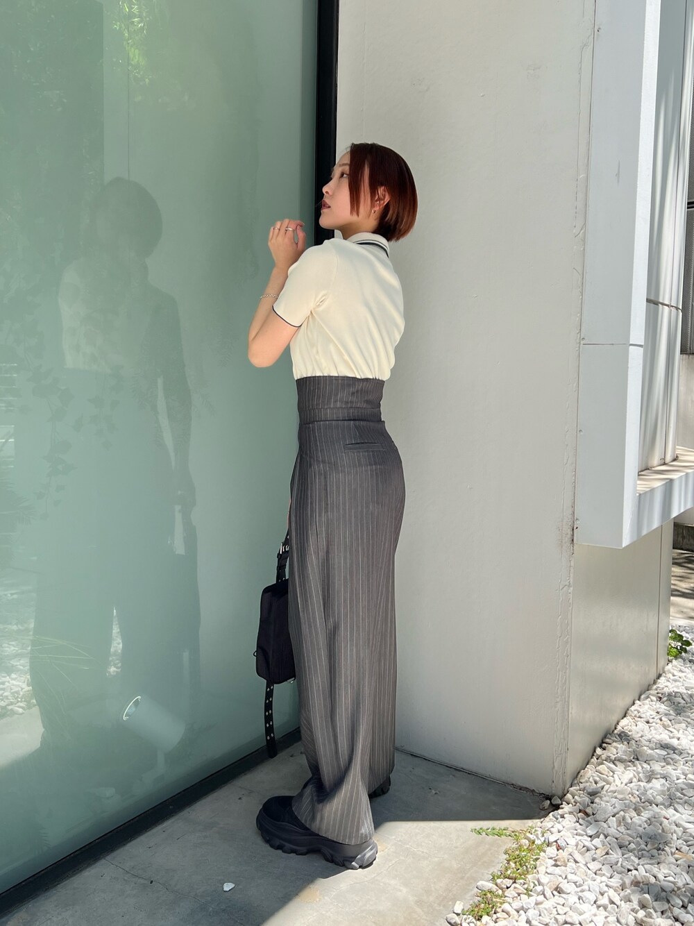 ホワイト系のポロシャツ、グレー系のスラックス、ブラック系のショルダーバッグを着用したレディースの夏コーディネートの1枚目の写真