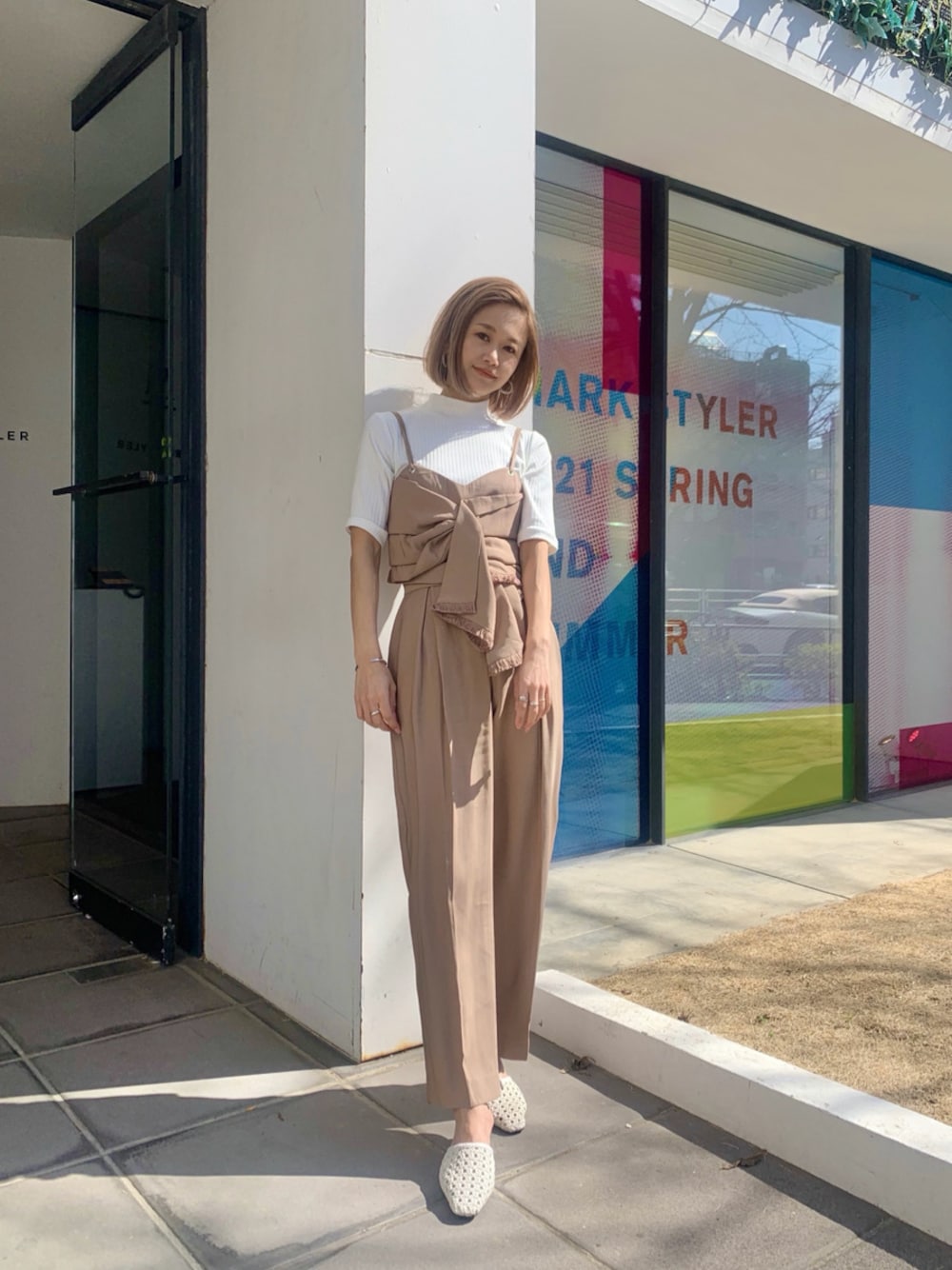 ベージュ系のスラックス、ホワイト系のサンダル、ベージュ系のTシャツ/カットソーを着用したレディースの春コーディネートの1枚目の写真