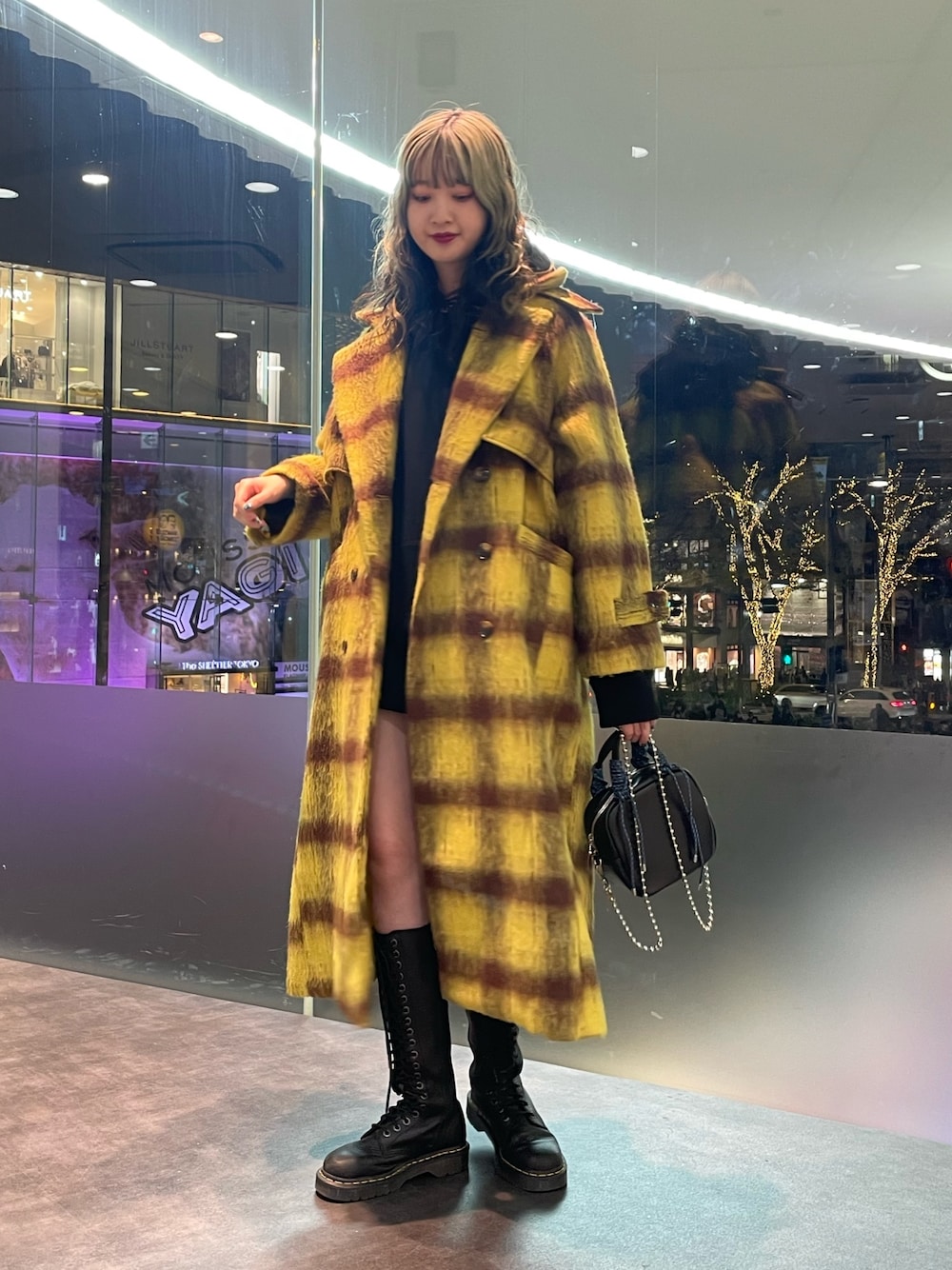 イエロー系のチェスターコート、ブラック系のパーカー、ブラック系のショルダーバッグを着用したレディースの冬コーディネートの1枚目の写真