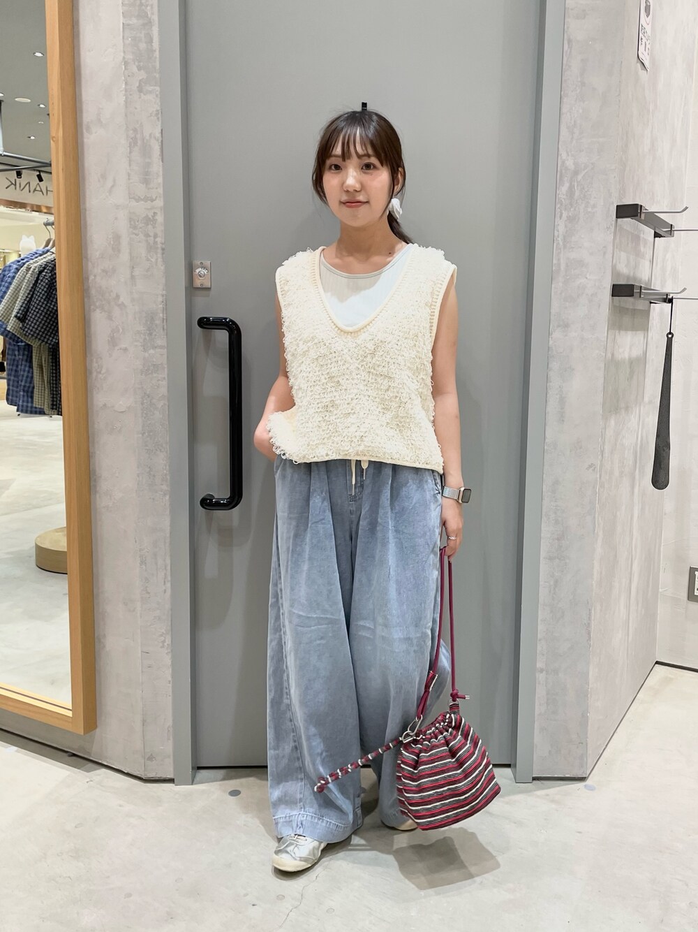 ホワイト系のベスト、ブルー系のデニムパンツ、レッド系のショルダーバッグを着用したレディースの夏コーディネートの1枚目の写真