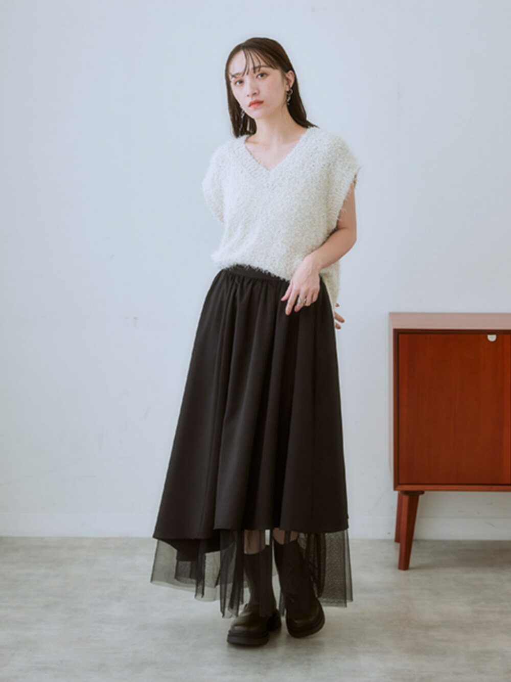 ブラック系のスカート、ベージュ系のニット/セーター、ホワイト系のキャミソールを着用したレディースの冬コーディネートの1枚目の写真