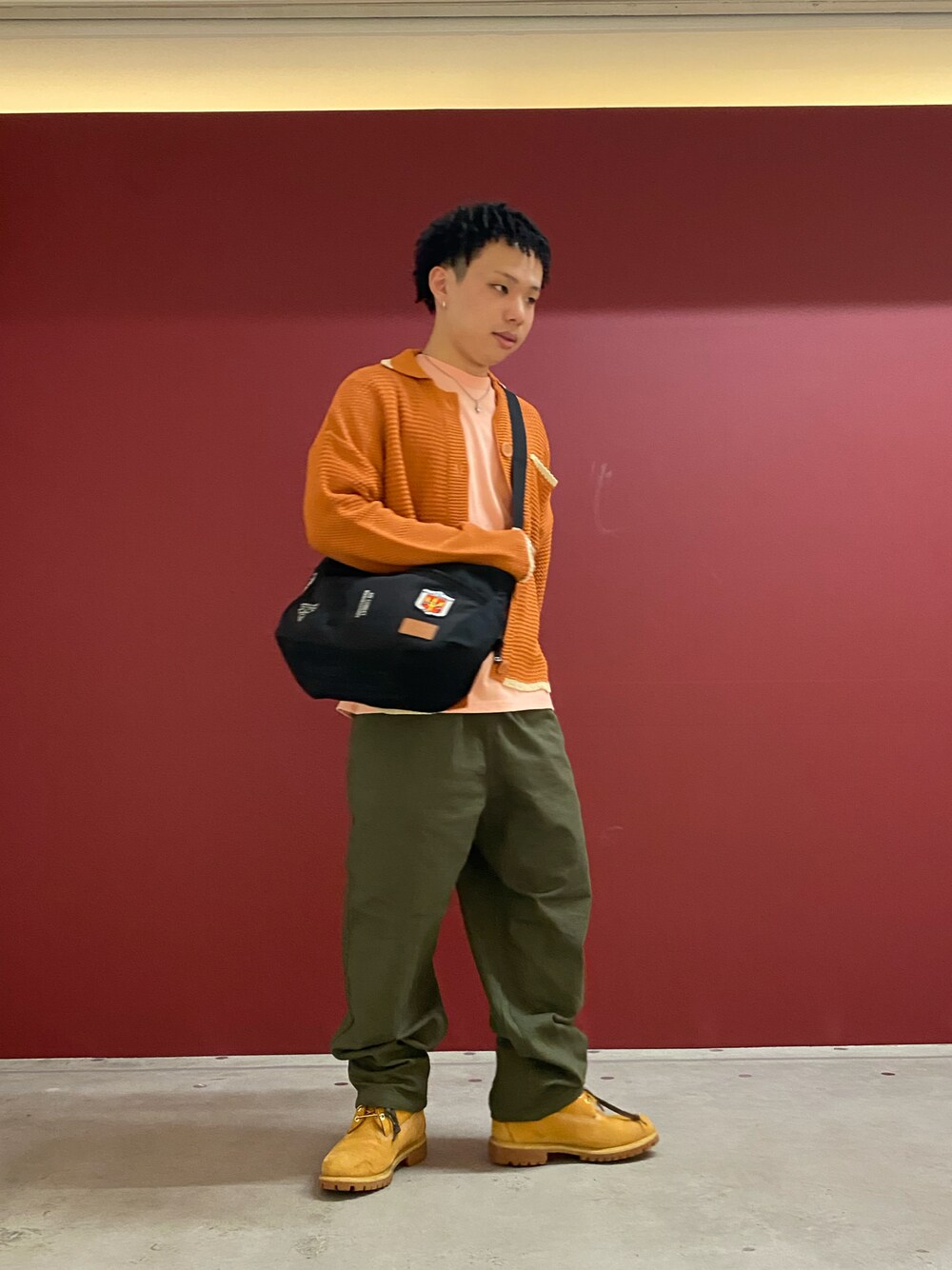 オレンジ系のカーディガン/ボレロ、ブラック系のショルダーバッグ、グリーン系のカーゴパンツを着用したメンズの春コーディネートの1枚目の写真