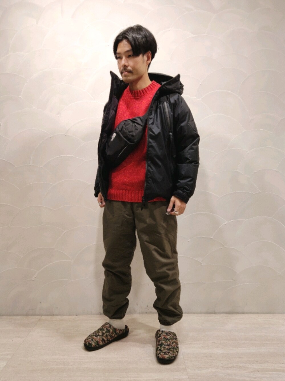 ブラック系のダウンジャケット/コート、ブラック系のボディバッグ/ウエストポーチ、オレンジ系のニット/セーターを着用したメンズの冬コーディネートの1枚目の写真