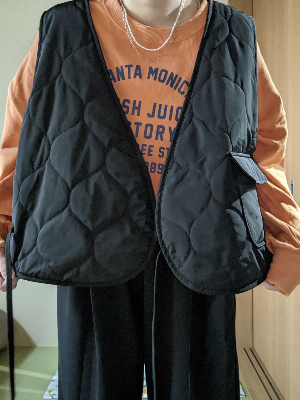 ブラック系のスウェットパンツ、ブラック系のベスト、オレンジ系のスウェットを着用したレディースの春コーディネートの3枚目の写真