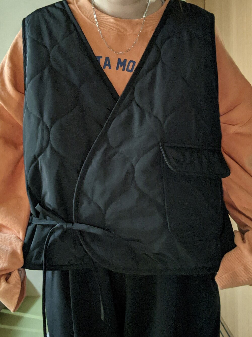 ブラック系のスウェットパンツ、ブラック系のベスト、オレンジ系のスウェットを着用したレディースの春コーディネートの4枚目の写真