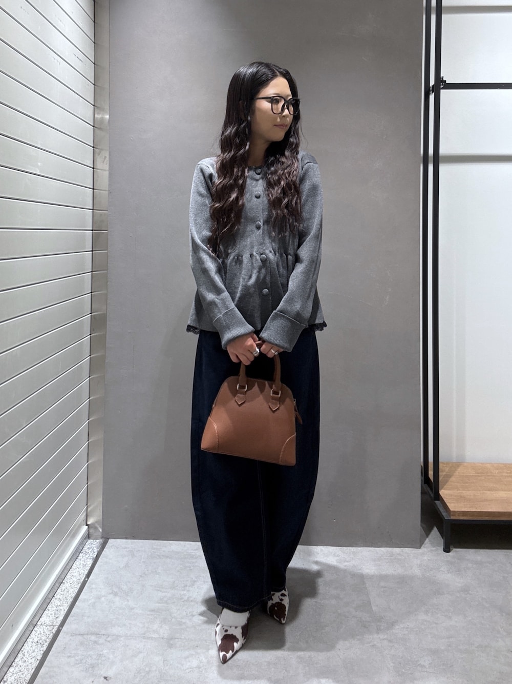 グレー系のニット/セーター、ブラウン系のショルダーバッグ、ブルー系のデニムパンツを着用したレディースの秋コーディネートの1枚目の写真