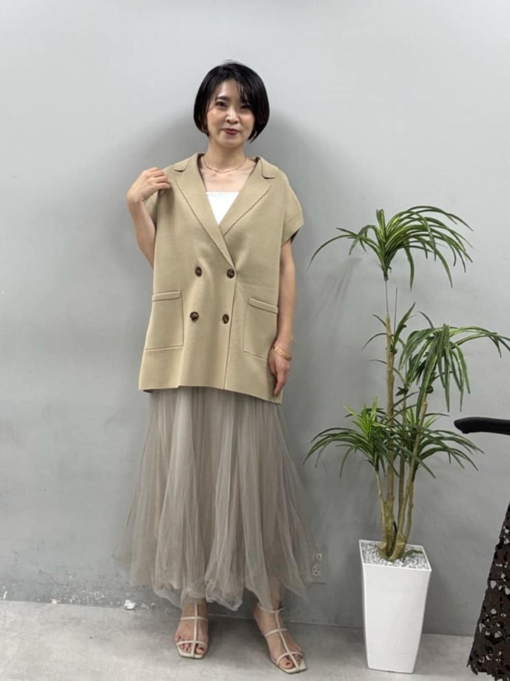 ホワイト系のキャミソール、ベージュ系のベスト、グレー系のスカートを着用したレディースの春コーディネートの1枚目の写真