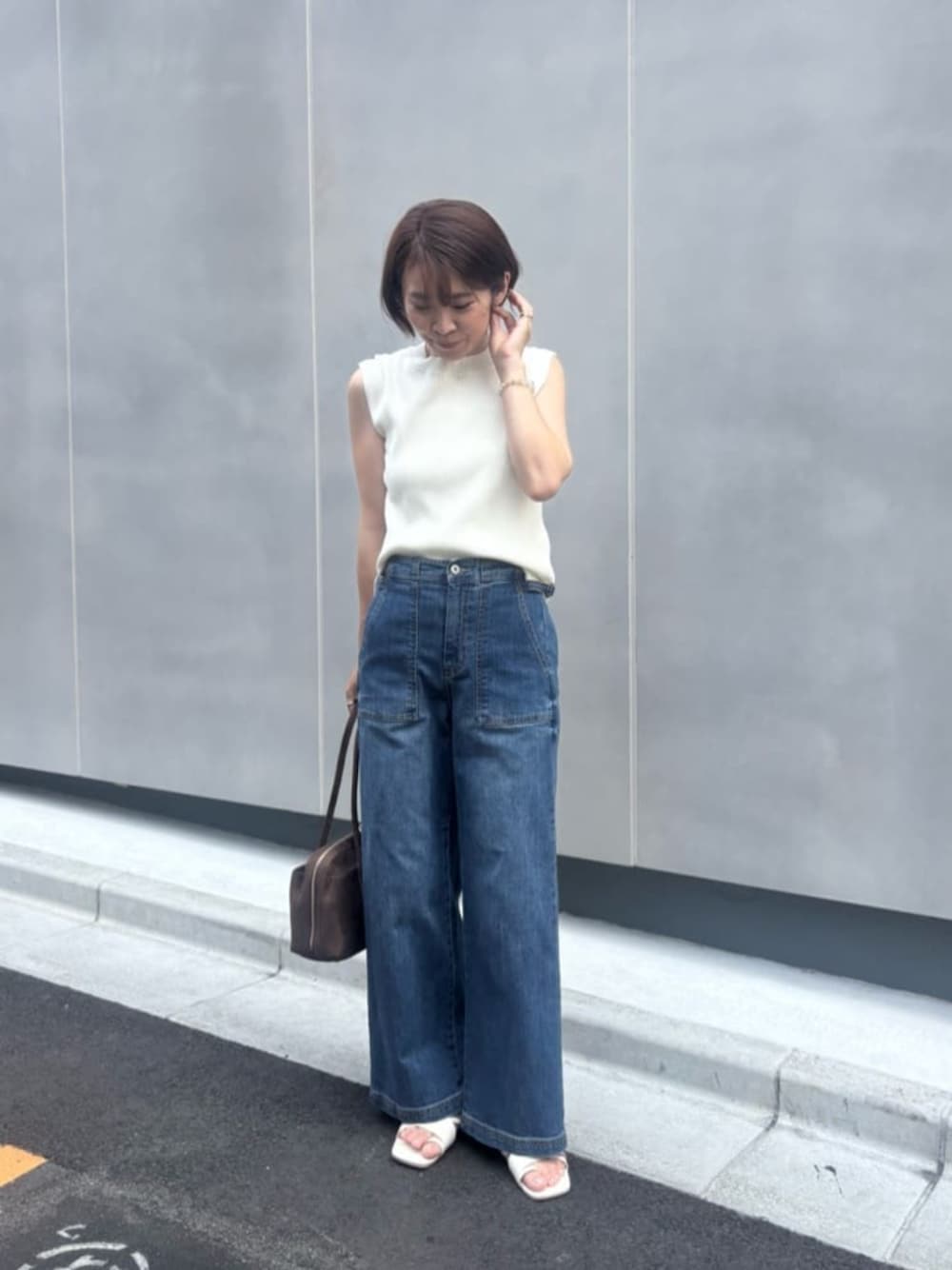 ホワイト系のニット/セーター、ブラウン系のボストンバッグ、ブルー系のデニムパンツを着用したレディースの夏コーディネートの1枚目の写真