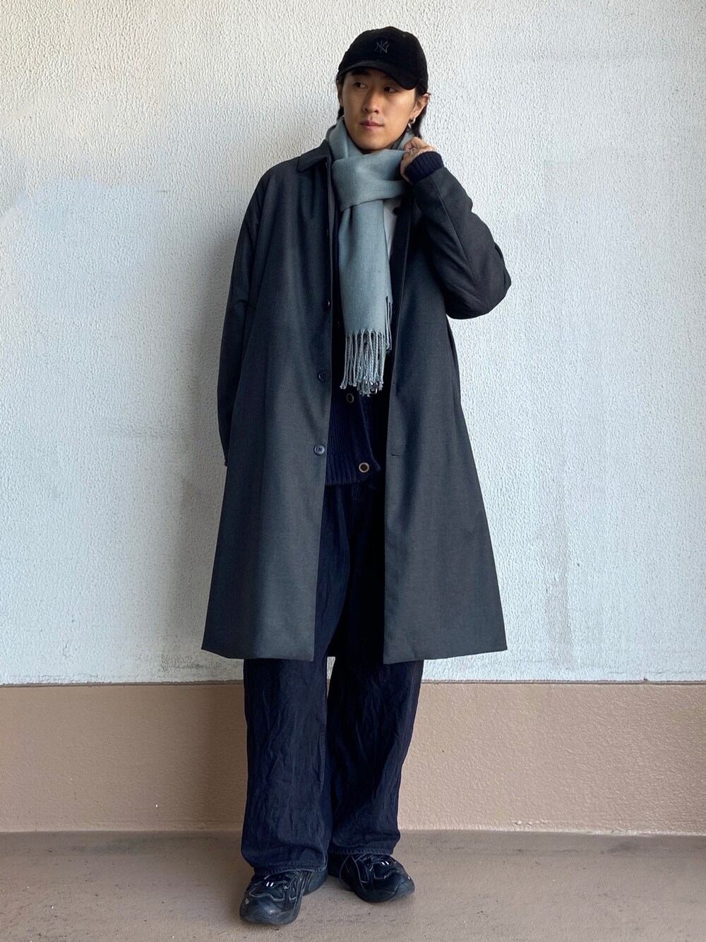 グレー系のステンカラーコート、ブラック系のデニムパンツ、グリーン系のマフラーを着用したメンズの秋コーディネートの1枚目の写真