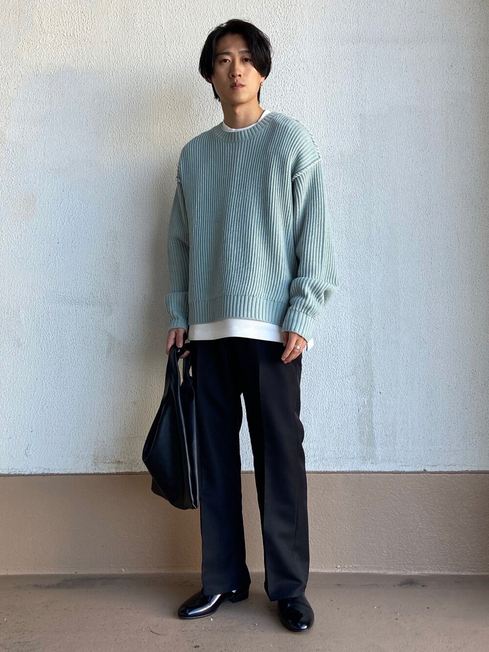 グリーン系のニット/セーター、ブラック系のトートバッグ、ブラック系のスラックスを着用したメンズの冬コーディネートの1枚目の写真