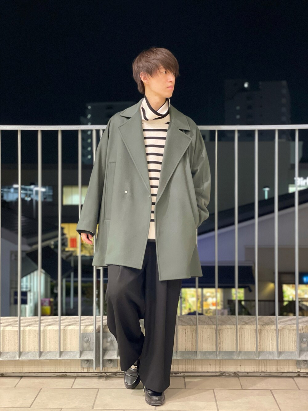 グリーン系のチェスターコート、ホワイト系のニット/セーター、ブラック系のスラックスを着用したメンズの秋コーディネートの1枚目の写真