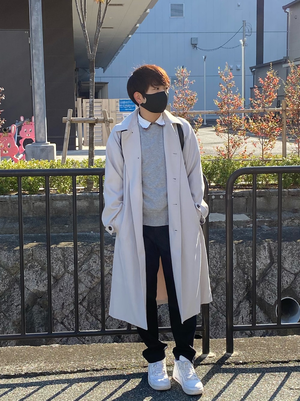 グレー系のステンカラーコート、ブラック系のスラックス、ホワイト系のスニーカーを着用したメンズの秋コーディネートの1枚目の写真