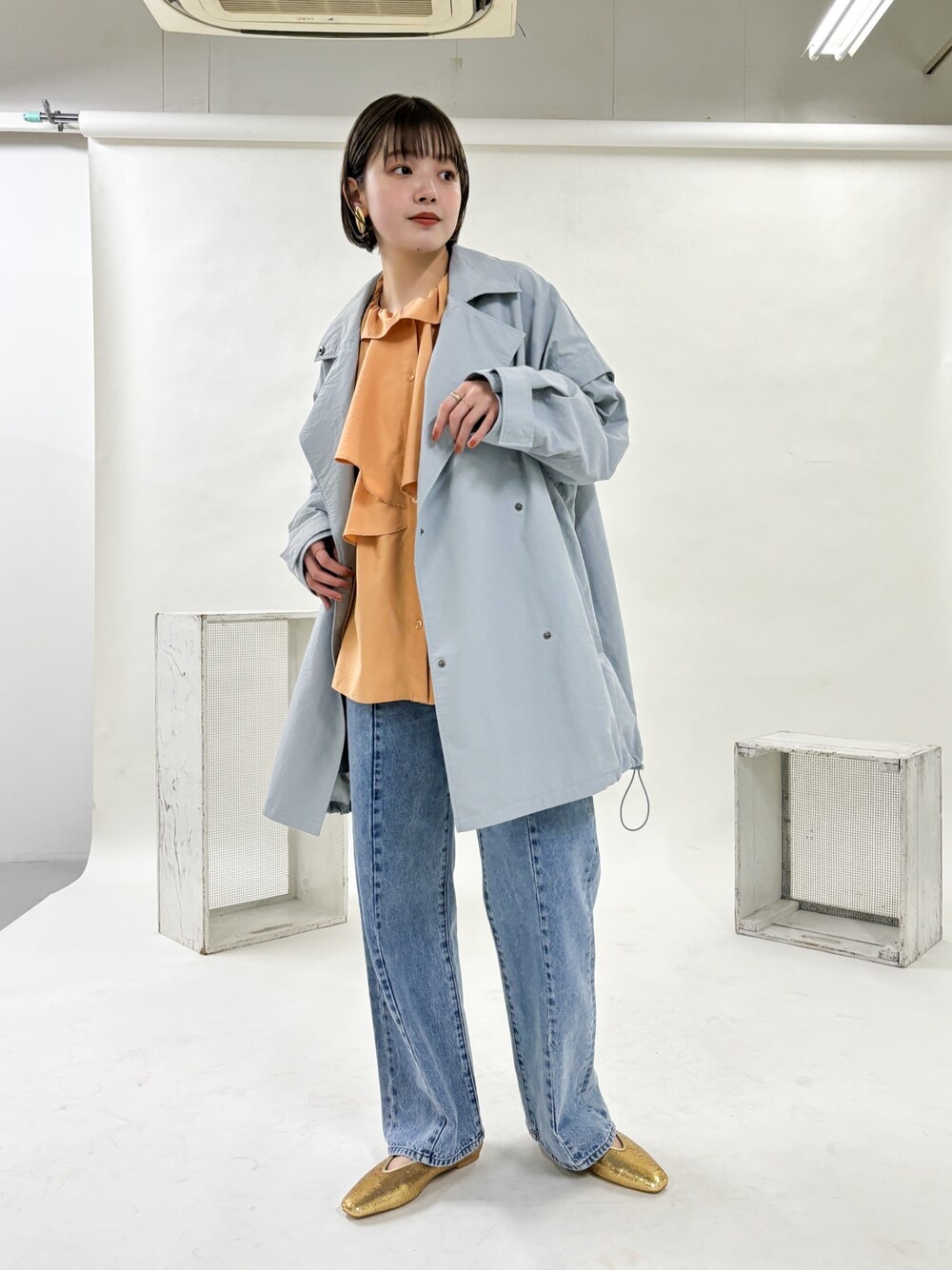 ブルー系のポンチョ、ブルー系のデニムパンツ、ゴールド系のパンプスを着用したレディースの冬コーディネートの1枚目の写真