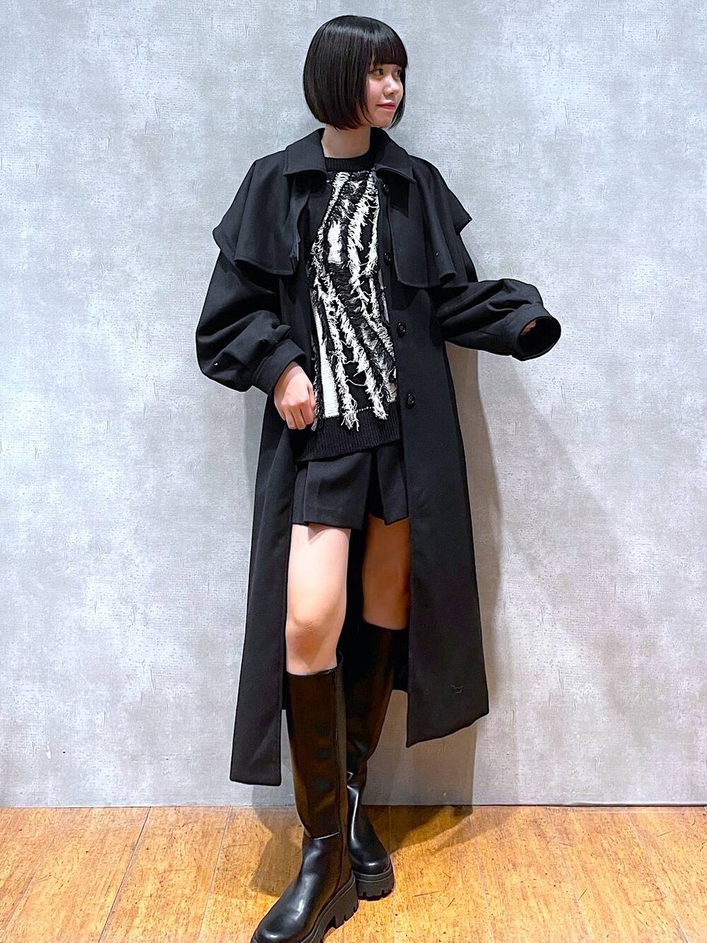 ブラック系のチェスターコート、ブラック系のブーツ、ブラック系のニット/セーターを着用したレディースの冬コーディネートの1枚目の写真